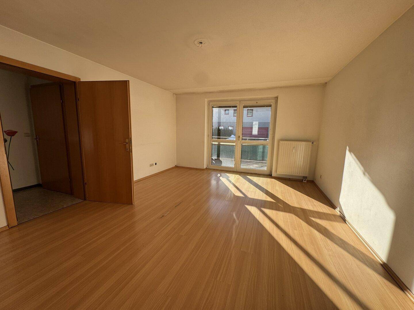 Helles Wohnzimmer mit Holzboden und Zugang zum Balkon, durchflutet von Sonnenlicht.