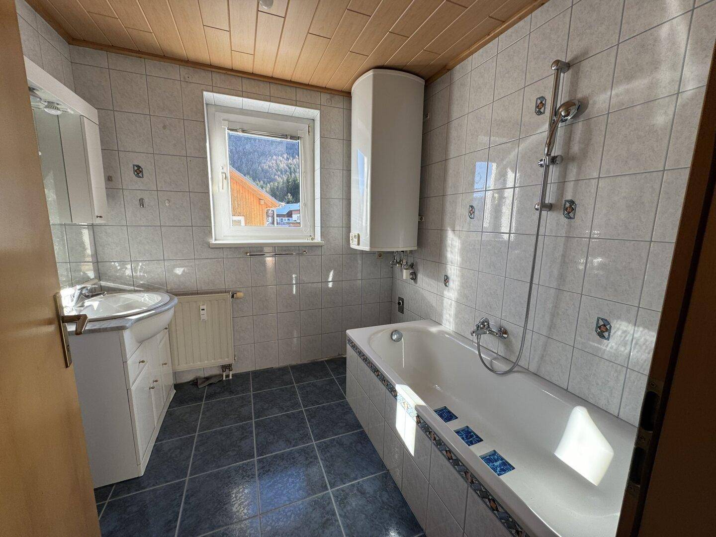 Badezimmer mit Badewanne, Waschbecken und Fenster, das einen Blick auf die Berge bietet.