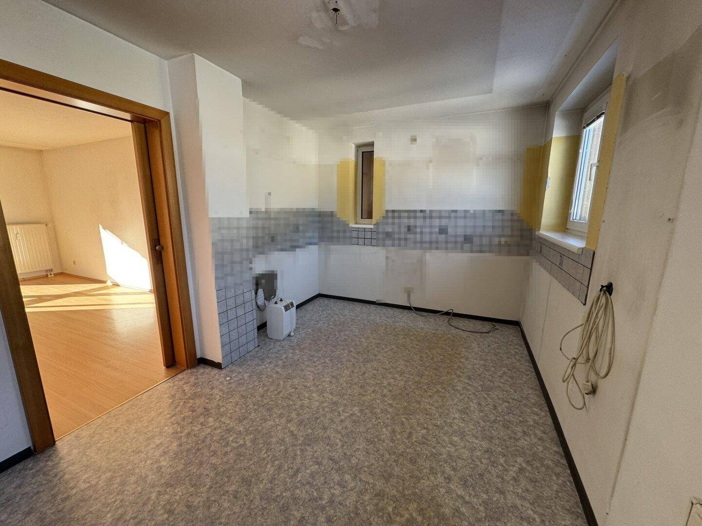 Leere Küche mit alten Fliesen und Blick in den angrenzenden Raum, bereit für eine Renovierung.