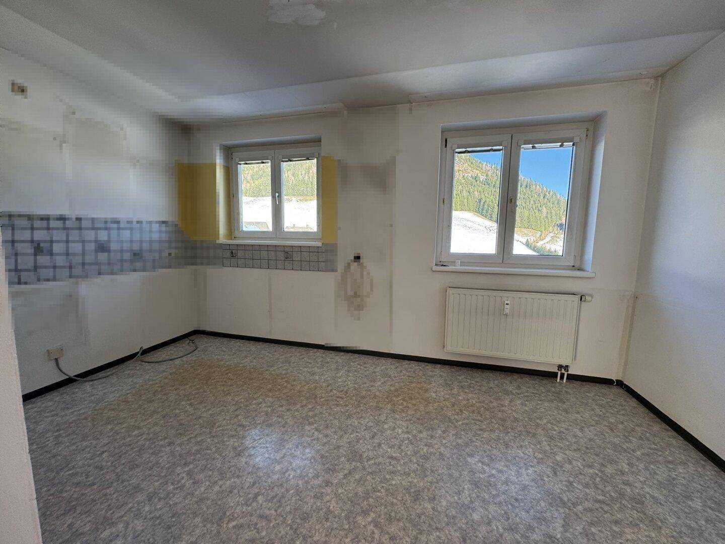 Leere Küche mit zwei Fenstern, die einen weiten Blick auf die verschneite Berglandschaft ermöglichen.