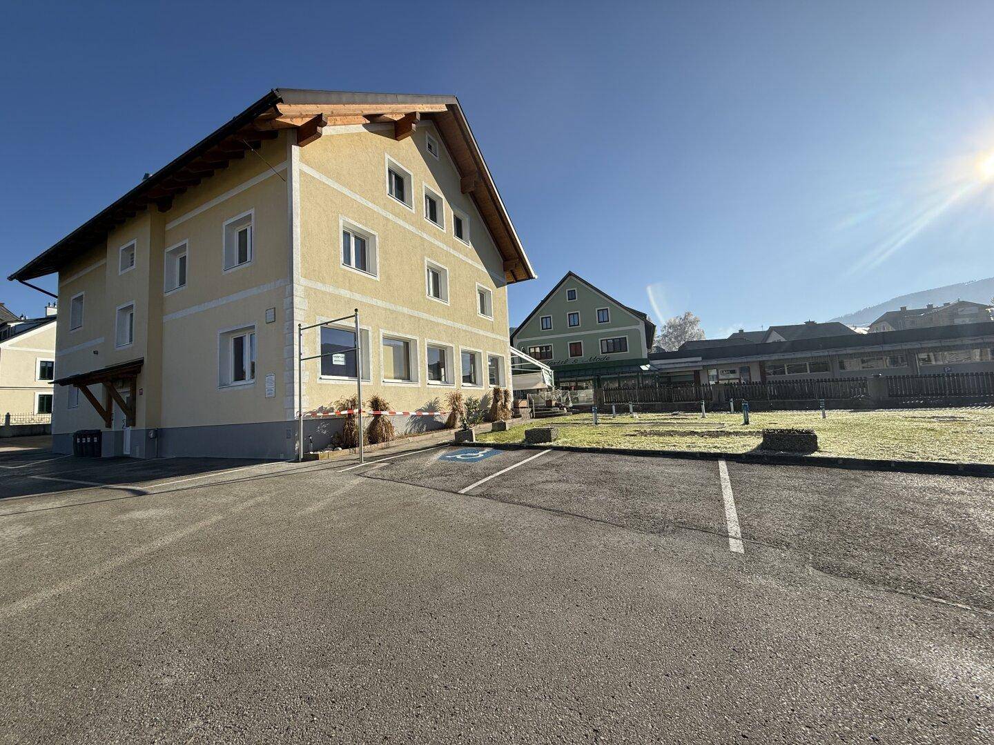 Seitenansicht des gelben Gebäudes mit großem asphaltierten Parkplatz unter strahlend blauem Himmel.