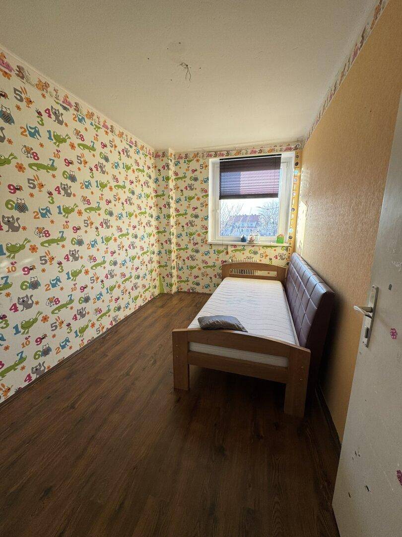Kinderzimmer mit einem Einzelbett und bunter, verspielter Tapete, die eine fröhliche Atmosphäre schafft.