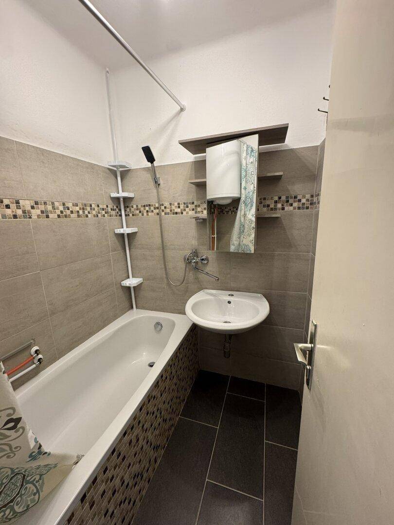 Badezimmer mit Badewanne, Waschbecken und modernen Fliesen in neutralen Farbtönen.