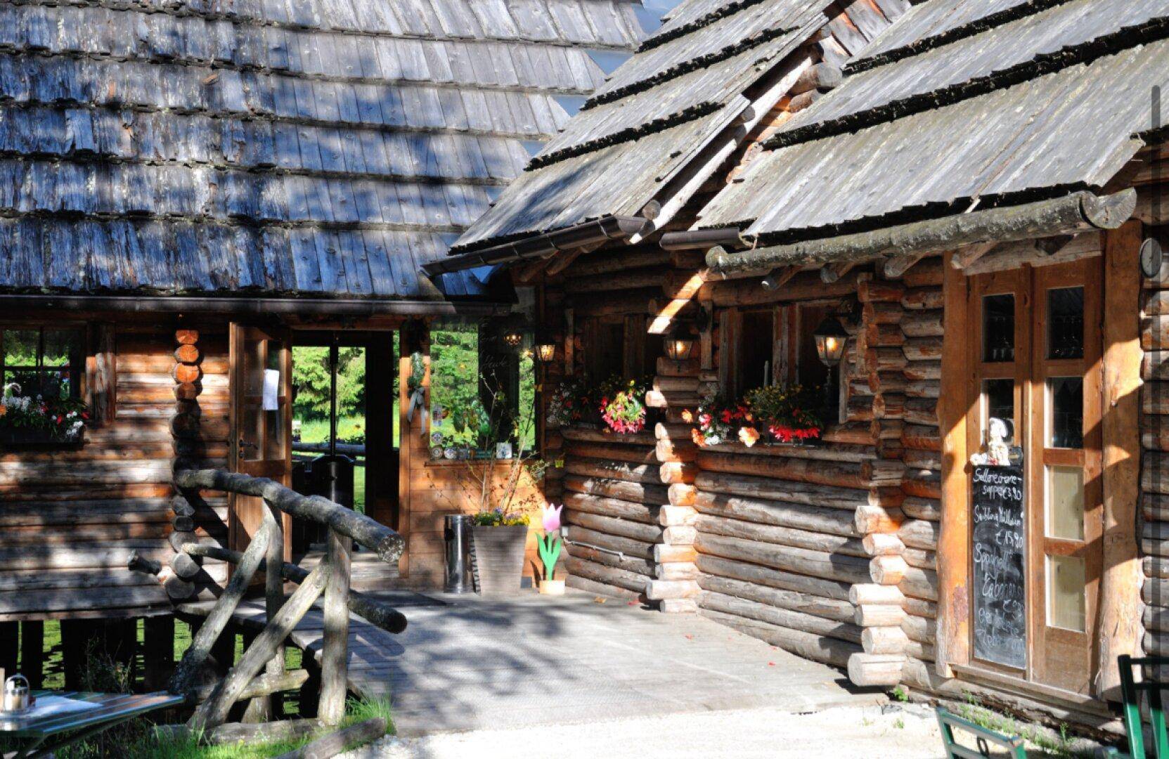 Detailansicht der rustikalen Blockhäuser mit Holzschindeldächern und Blumenkästen, die den Eingangsbereich schmücken.
