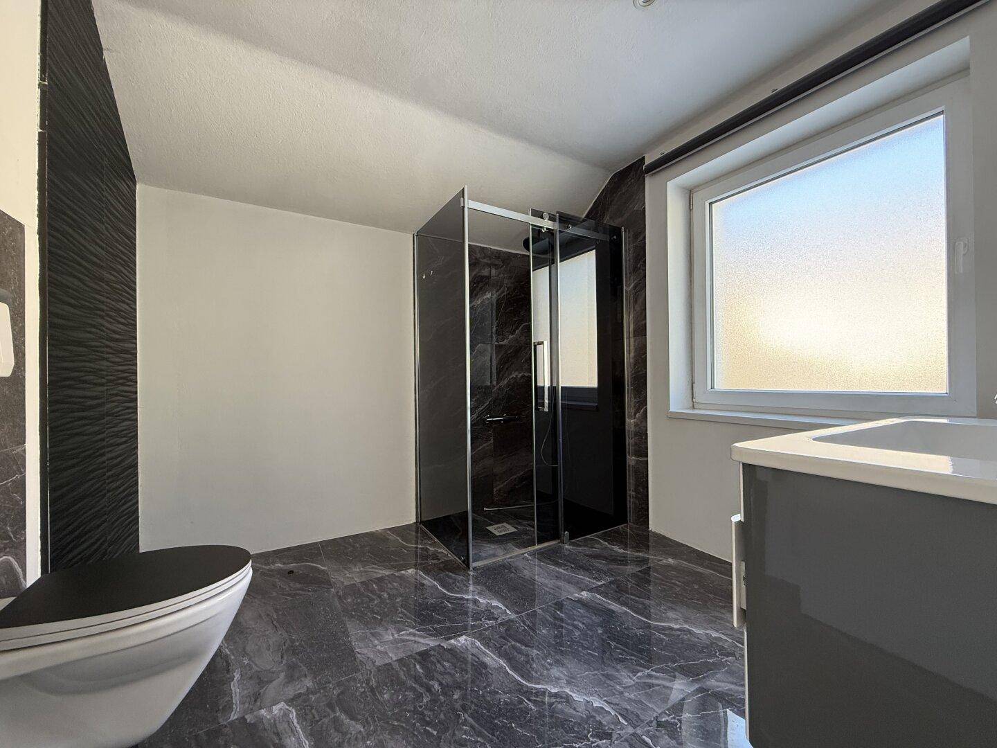 Modernes Badezimmer mit dunklen Marmorfliesen, begehbarer Dusche und Wand-WC.