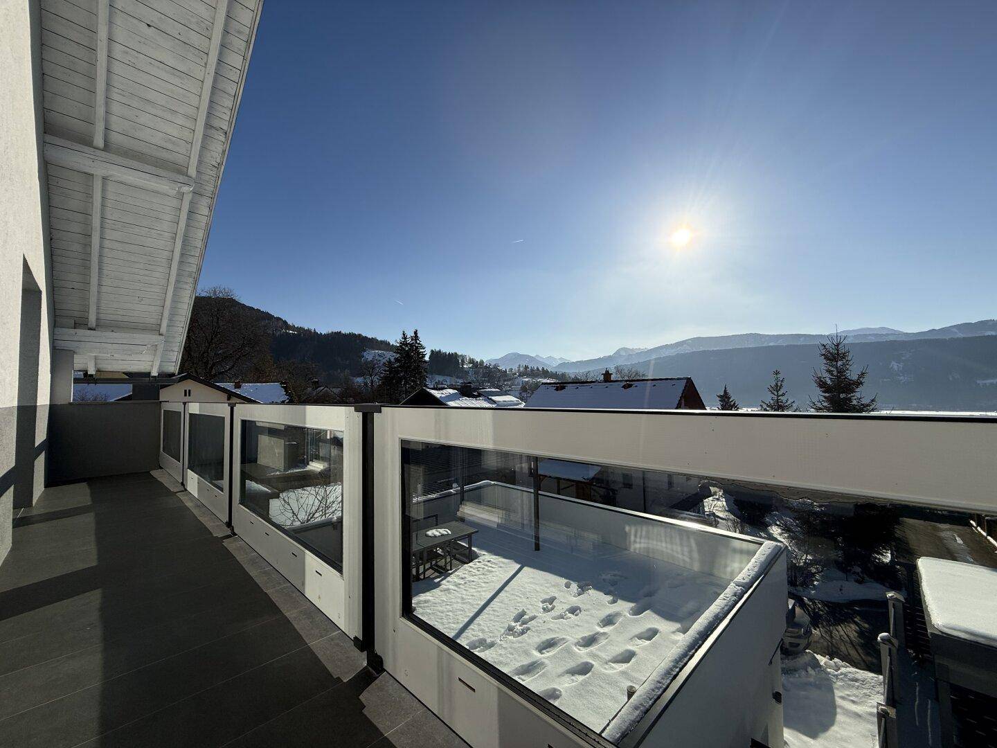 Heller Balkon mit weitem Blick über die schneebedeckten Dächer und die umliegende Bergwelt.