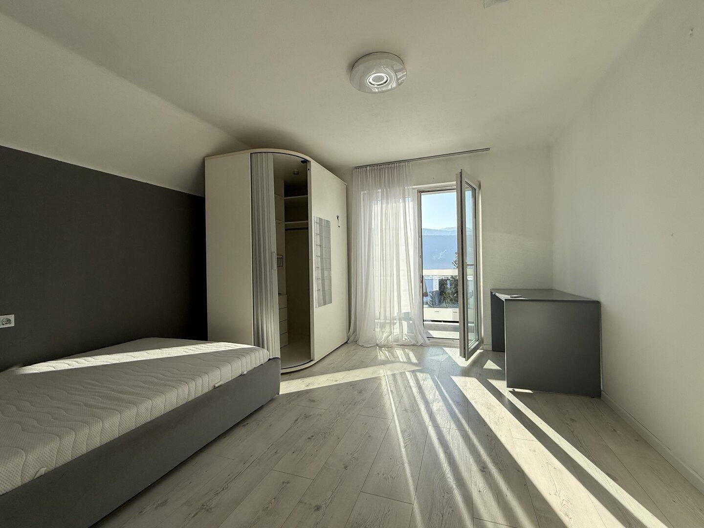 Helles Schlafzimmer mit Balkonzugang, Einzelbett und Schreibtisch, mit Blick auf die Berge.