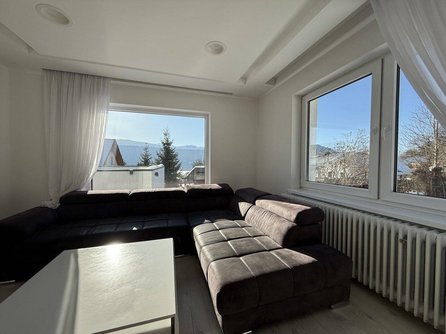 Lichtdurchflutetes Wohnzimmer mit großen Fenstern und Blick auf die verschneite Landschaft.