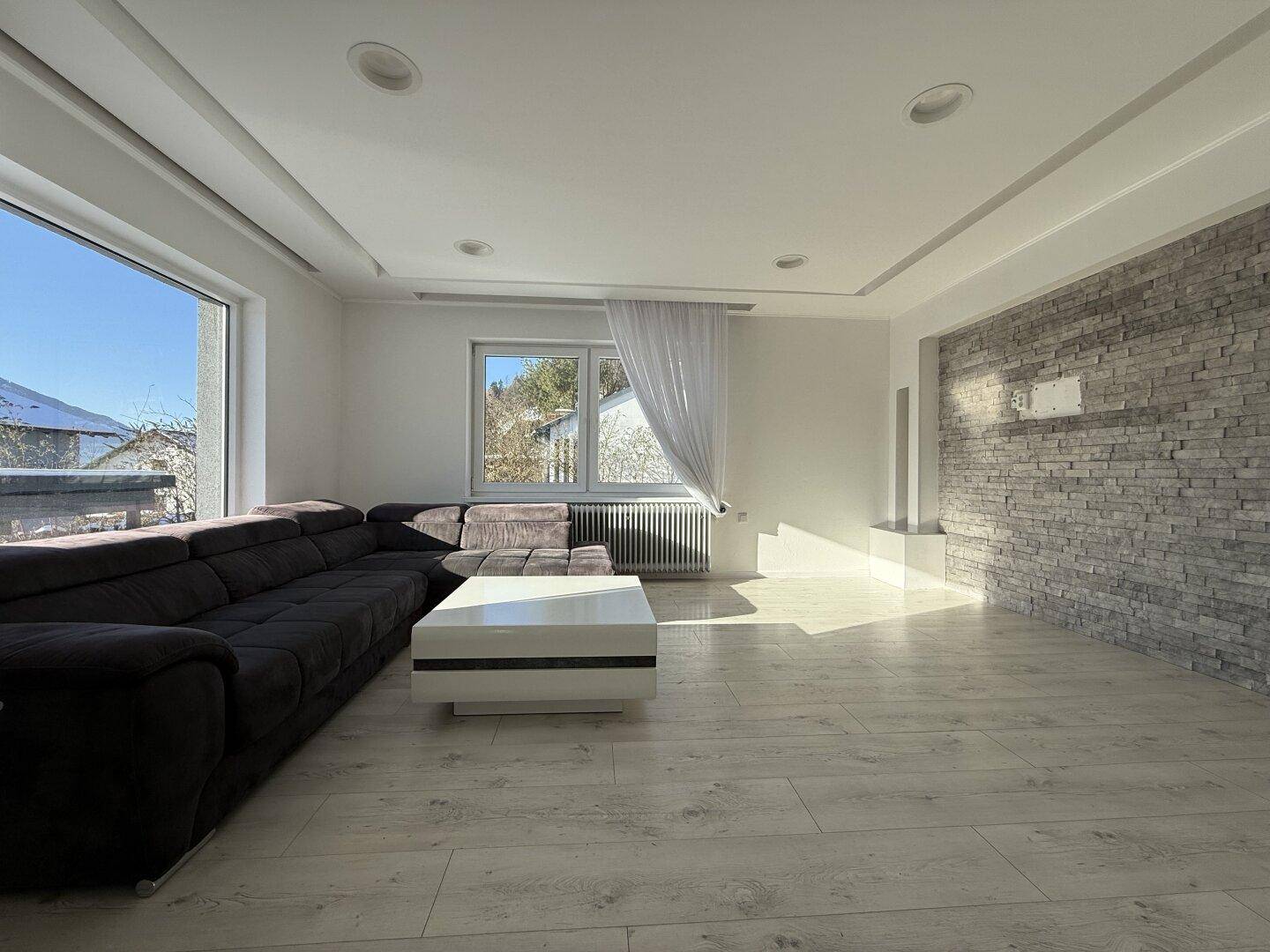 Helles Wohnzimmer mit großem Ecksofa, modernem Couchtisch und Steinwandakzent.