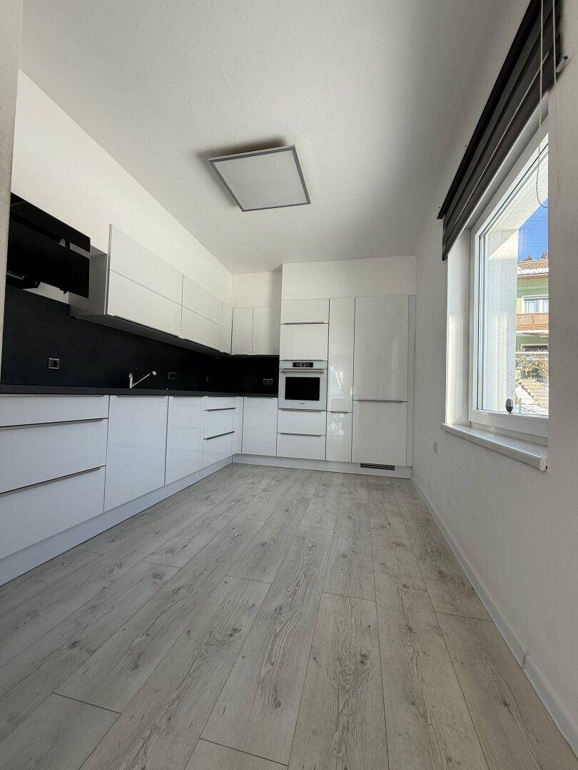 Moderne, helle Küche mit weißen Hochglanzfronten, integrierten Geräten und Laminatboden.
