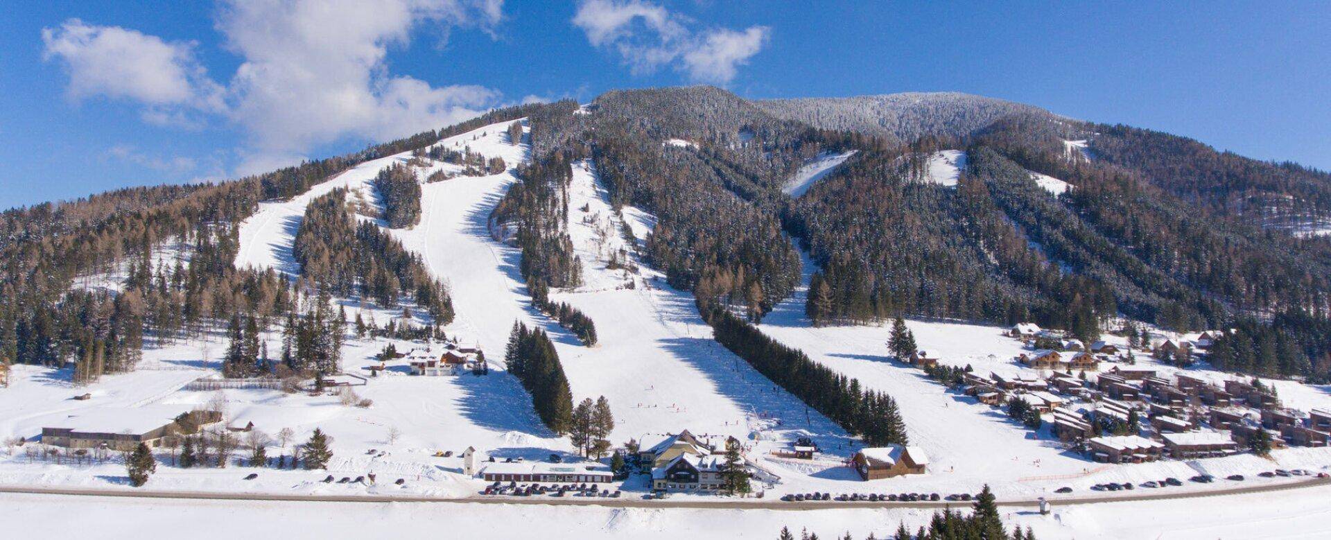 Weitläufige Panoramaansicht des Skigebiets mit zahlreichen Pisten und umliegenden Gebäuden.