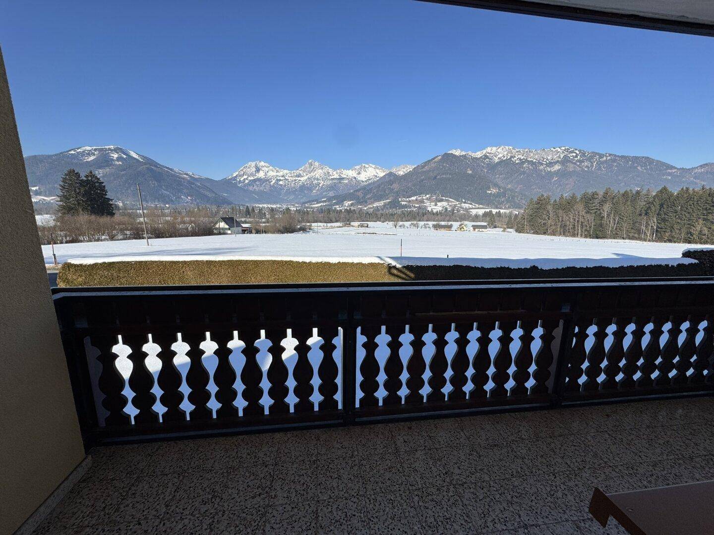 Blick vom Balkon auf eine weite, schneebedeckte Landschaft mit beeindruckenden Bergen unter blauem Himmel.