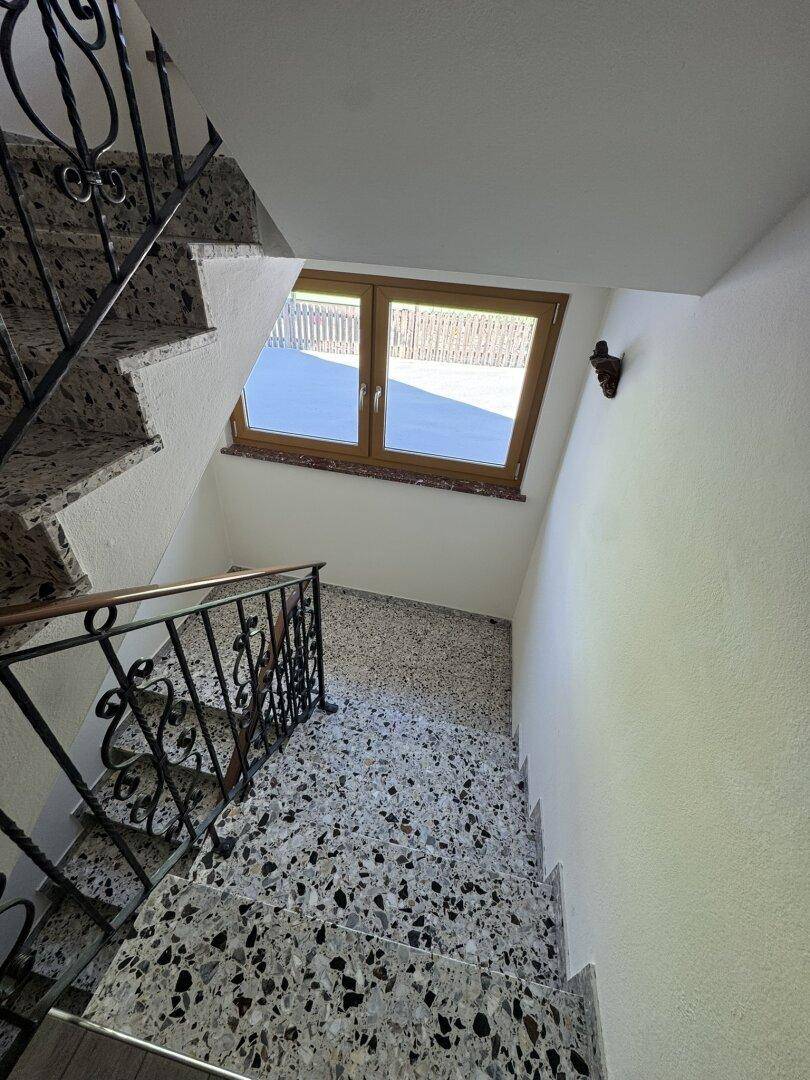 Treppenhaus mit Terrazzostufen, schmiedeeisernem Geländer und einem Fenster für natürliches Licht.