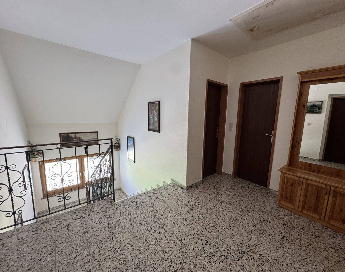 Heller Flur mit Terrazzoboden und einer Treppe mit schmiedeeisernem Geländer, die in die oberen Stockwerke führt.