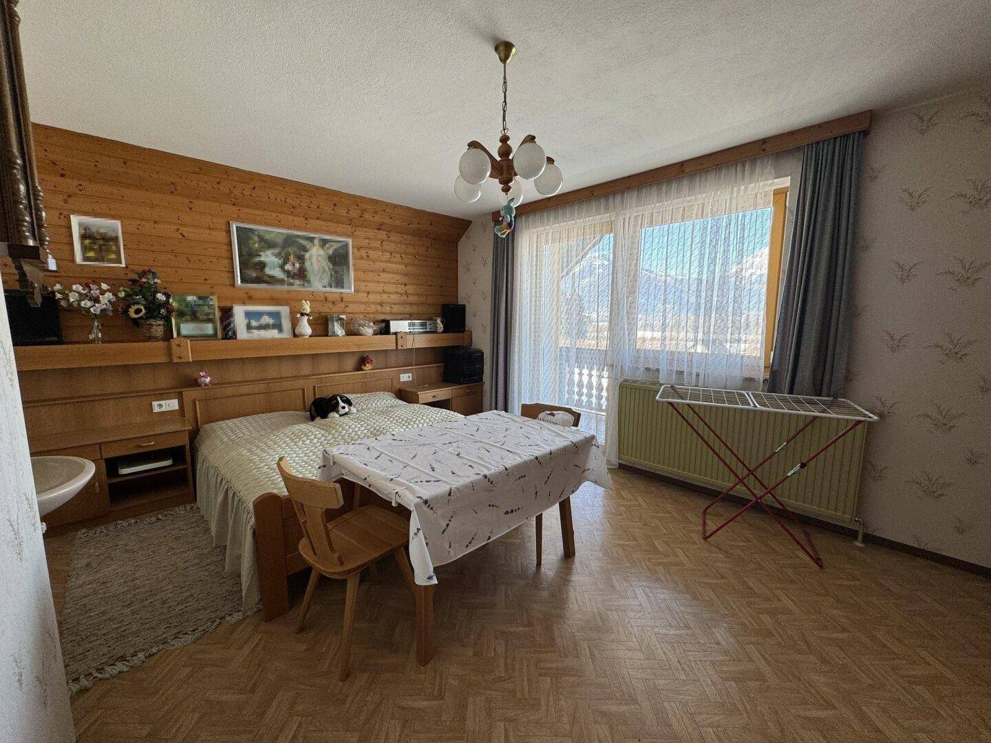 Schlafzimmer mit Holzvertäfelung, Parkettboden und Zugang zu einem Balkon mit Bergblick.