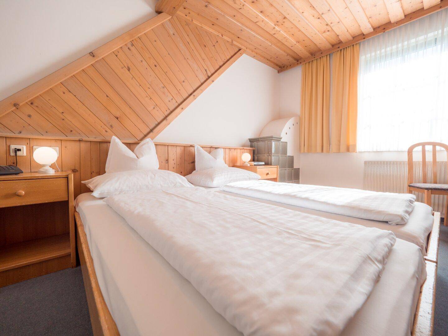 Gemütliches Schlafzimmer mit zwei Einzelbetten, Holzdecke und traditionellem Kachelofen.