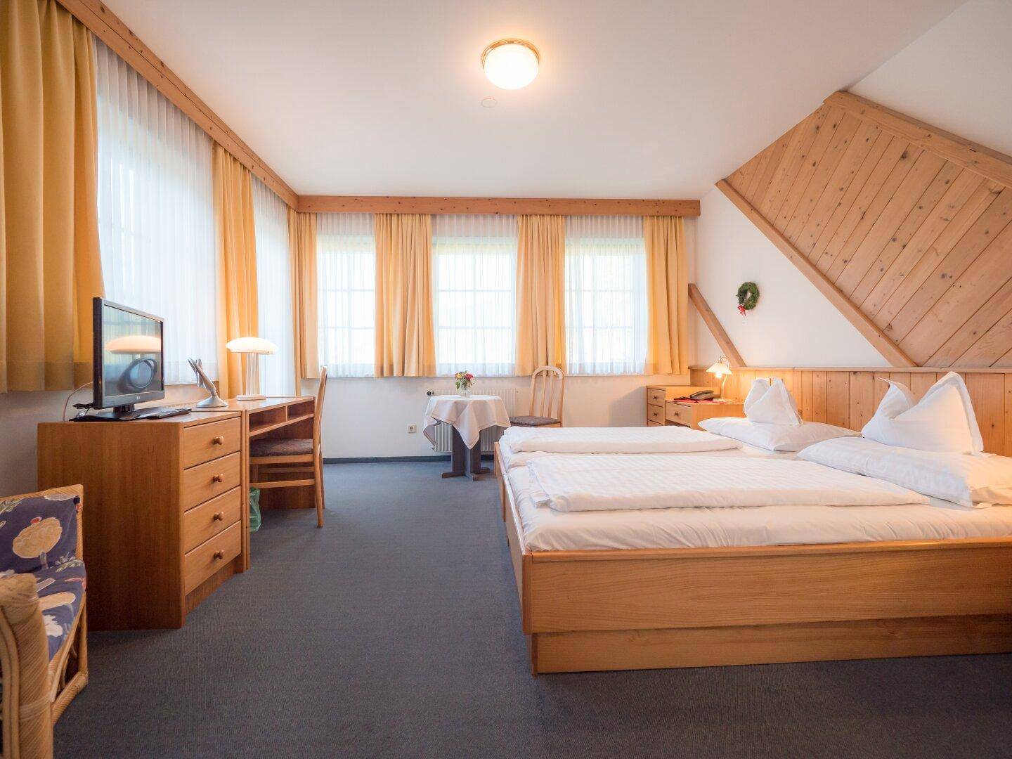 Helles Schlafzimmer mit zwei Einzelbetten, Holzdecke, Schreibtisch und Teppichboden.