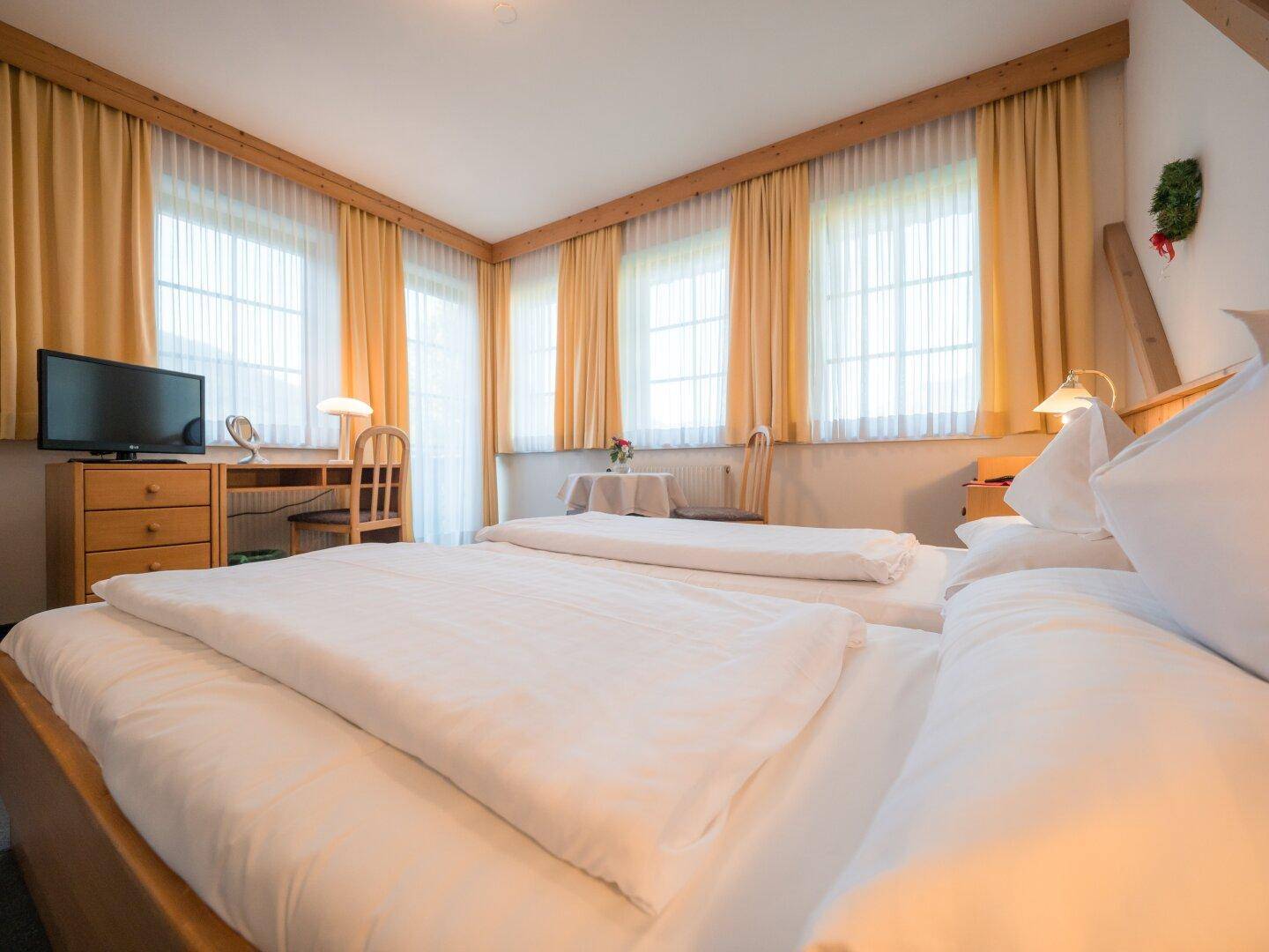 Freundliches Schlafzimmer mit zwei Einzelbetten, Holzmöbeln und Blick auf die Fensterfront.