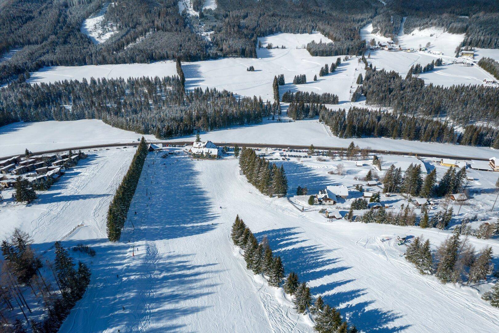Winterliche Landschaft aus der Vogelperspektive mit verschneiten Feldern, Wäldern und vereinzelten Häusern.