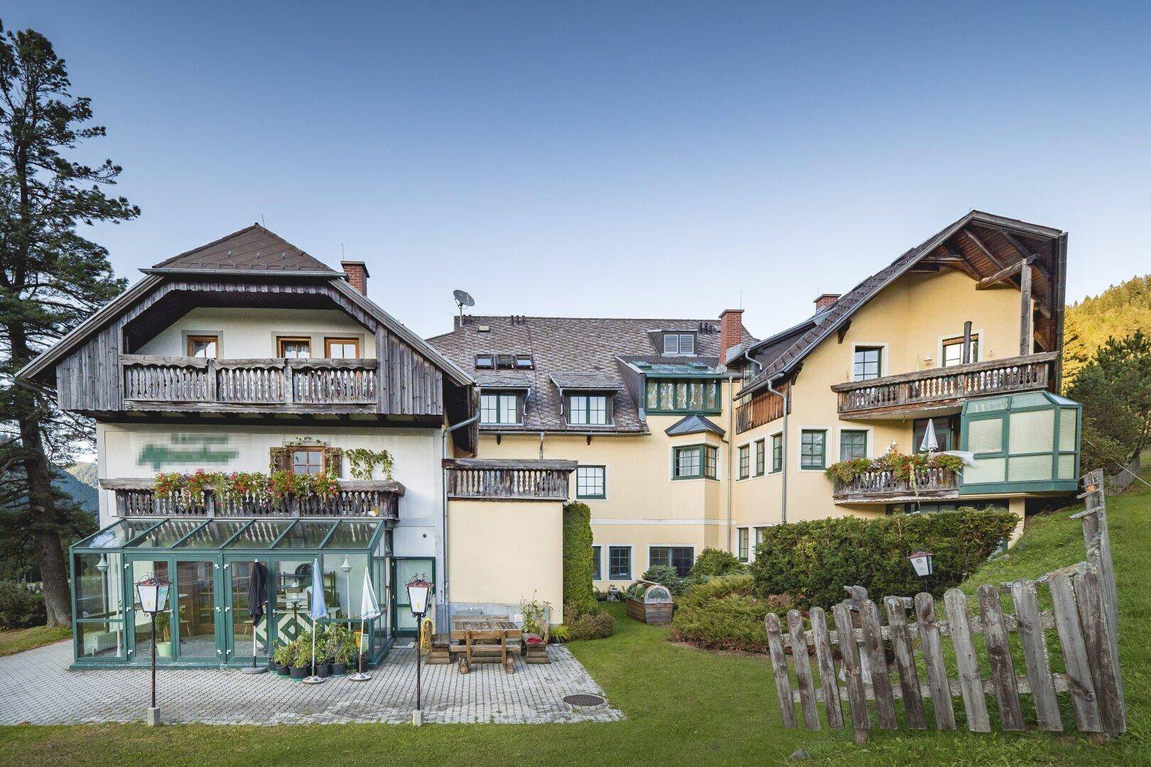 Hotelgebäude im Sommer mit grüner Gartenanlage, Außenterrasse und Sitzgelegenheiten.
