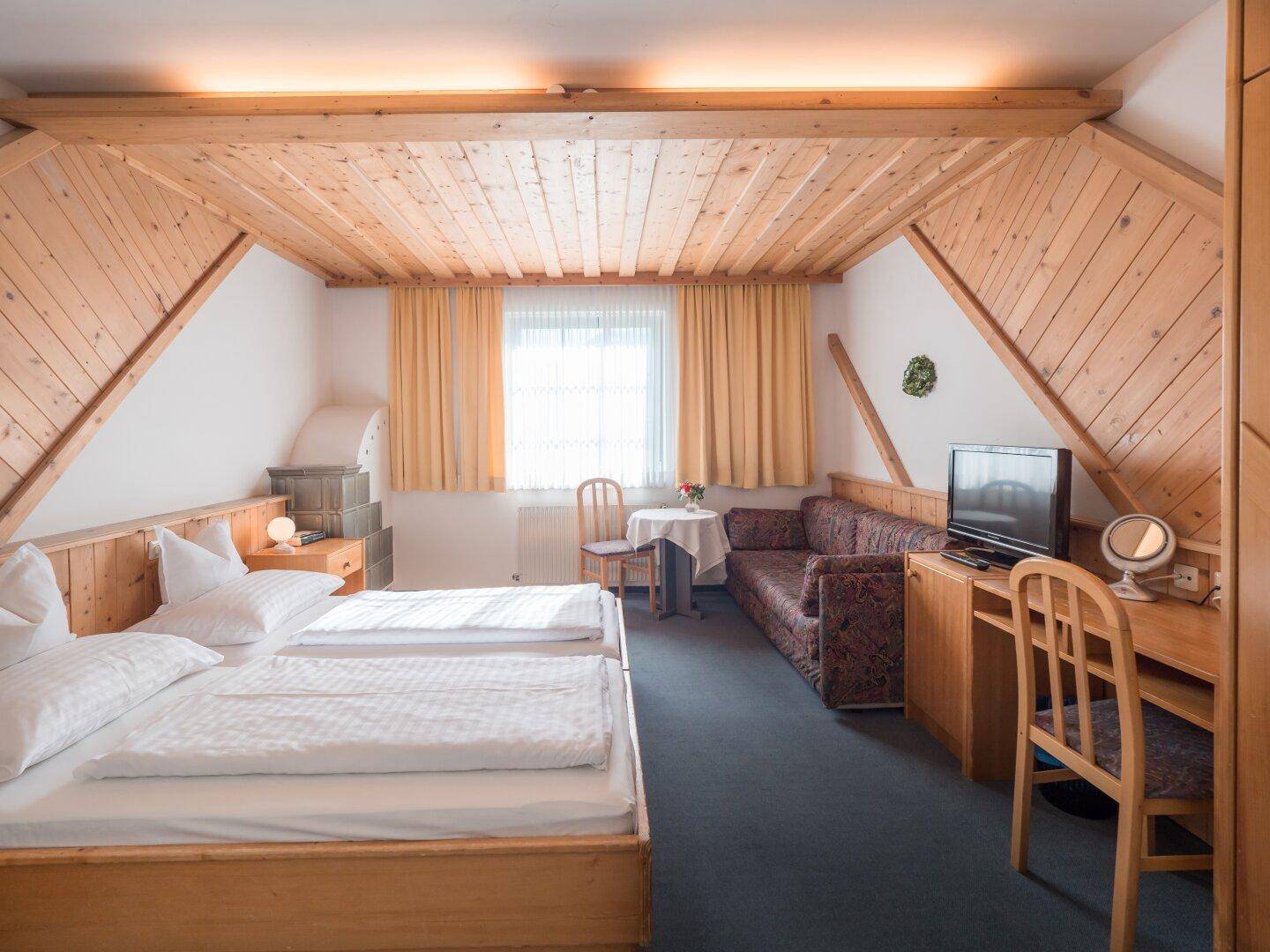 Geräumiges Schlafzimmer mit zwei Einzelbetten, Holzdecke, Schreibtisch und gemütlichem Sofa.