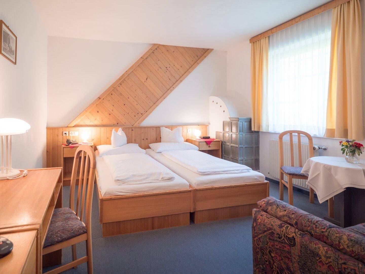 Komfortables Schlafzimmer mit zwei Einzelbetten, Holzmöbeln und einem traditionellen Kachelofen.