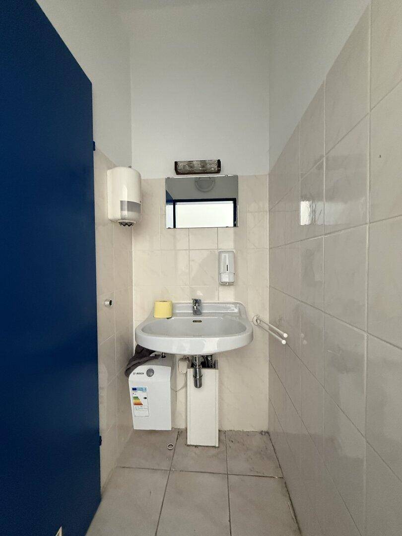 Badezimmer mit Waschbecken, Spiegel und Fliesen an den Wänden, inklusive Haltegriffen und Spiegelschrank.