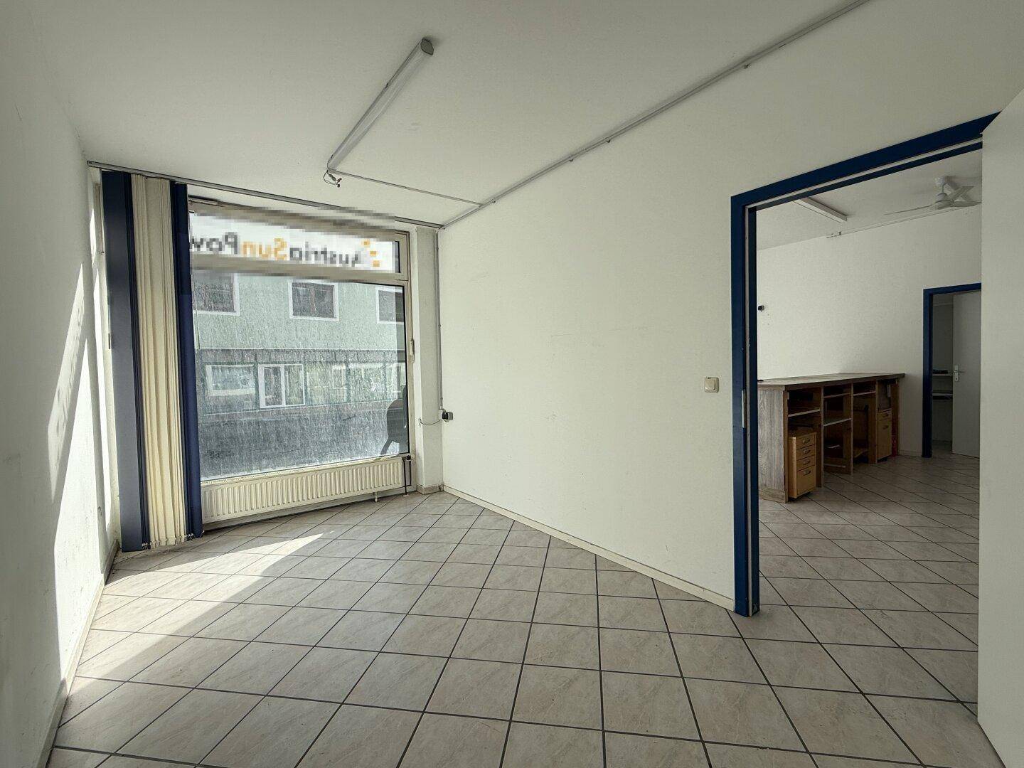 Heller Büroraum mit Fliesenboden, großen Fenstern und Blick auf die Straße, ausgestattet mit Deckenventilator.