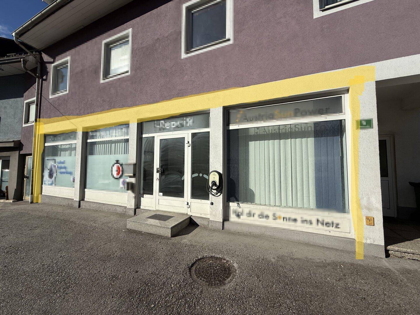 Gebäudefassade mit Geschäftsfronten im Erdgeschoss und einer Ladestation für Elektrofahrzeuge.