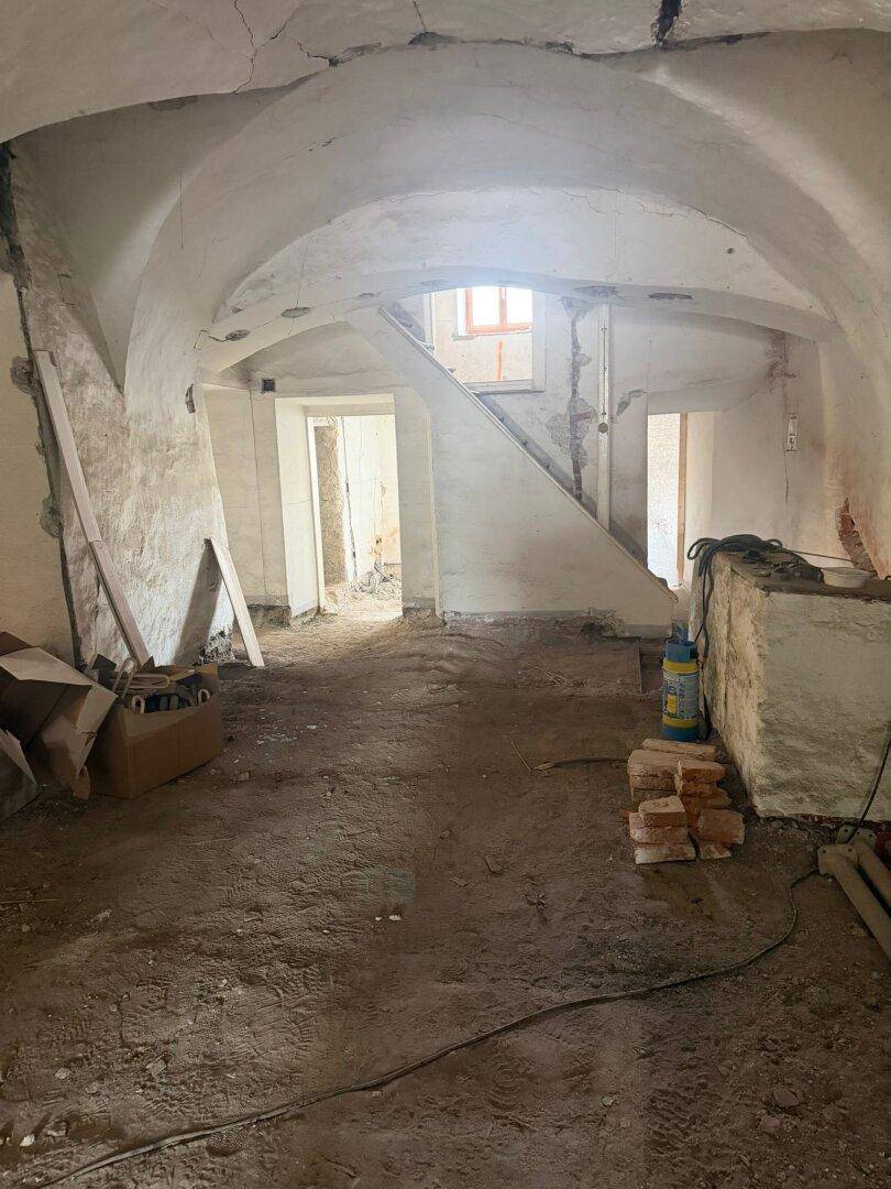 Großer Raum im Rohbau mit gewölbter Decke, einem Fenster und sichtbaren Bauarbeiten.