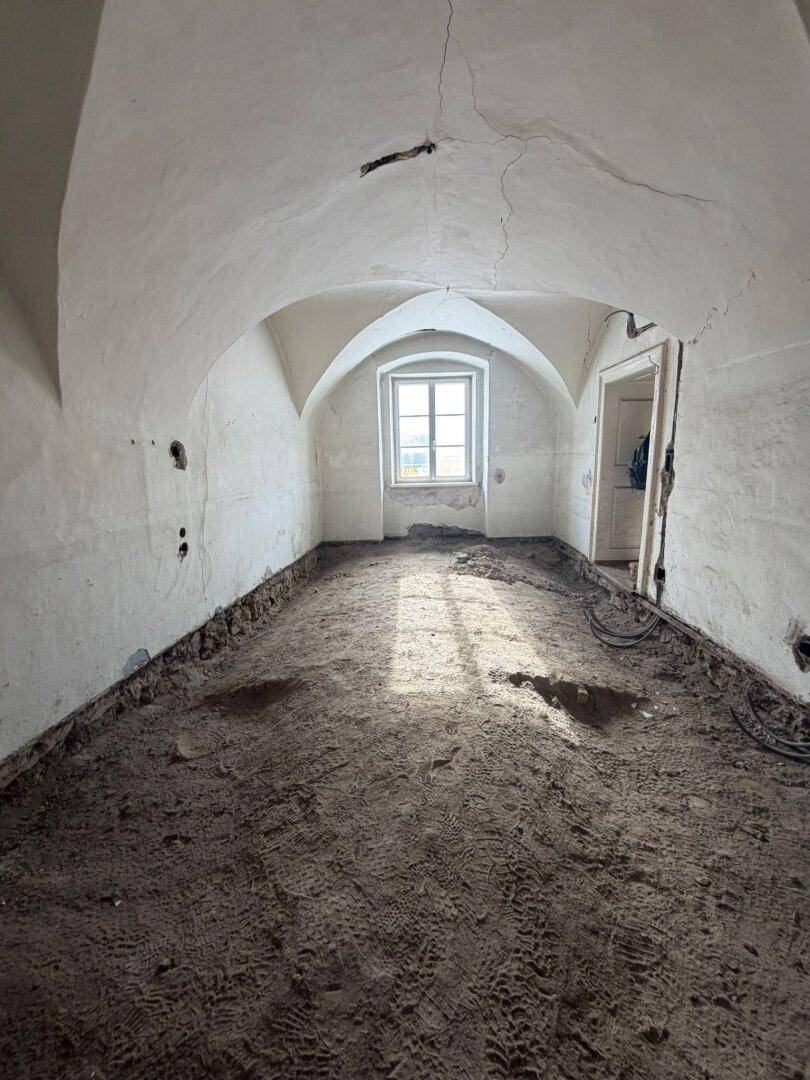 Raum im Rohbau mit gewölbter Decke, einem Fenster und vorbereitetem Boden für den Ausbau.