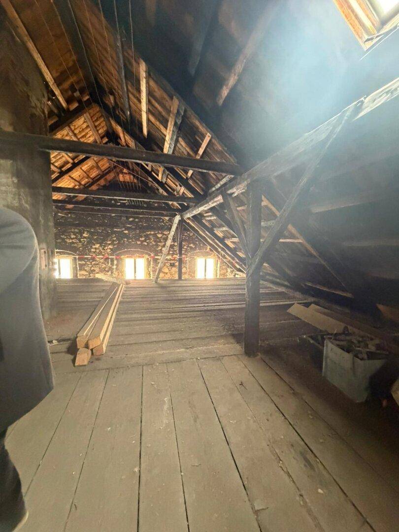 Großer Dachboden mit freiliegenden Holzbalken und mehreren Fenstern, bereit für den Ausbau.