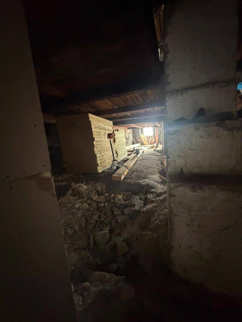 Dunkler Bereich im Rohbau mit Baumaterialien und einem Fenster in der Ferne.