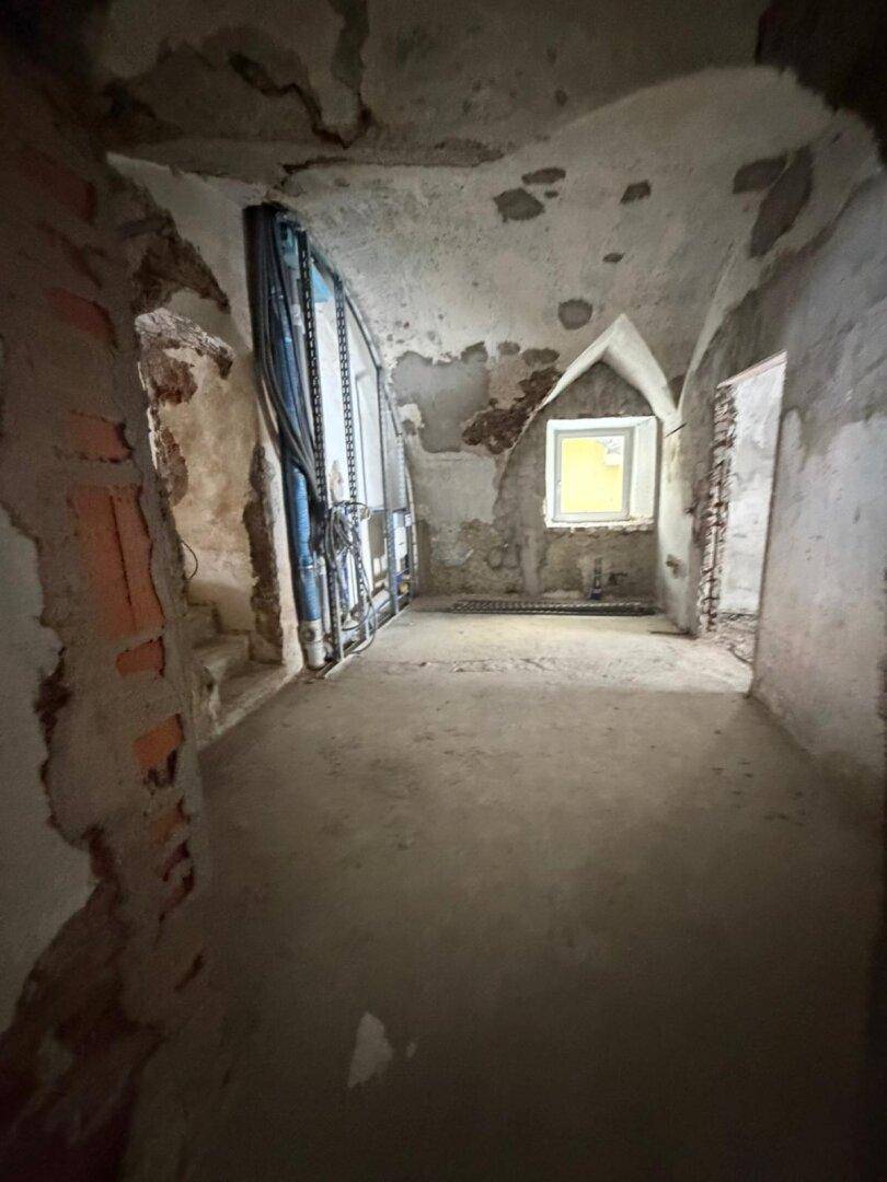Raum im Rohbau mit gewölbter Decke, einem Fenster und sichtbaren Renovierungsspuren.