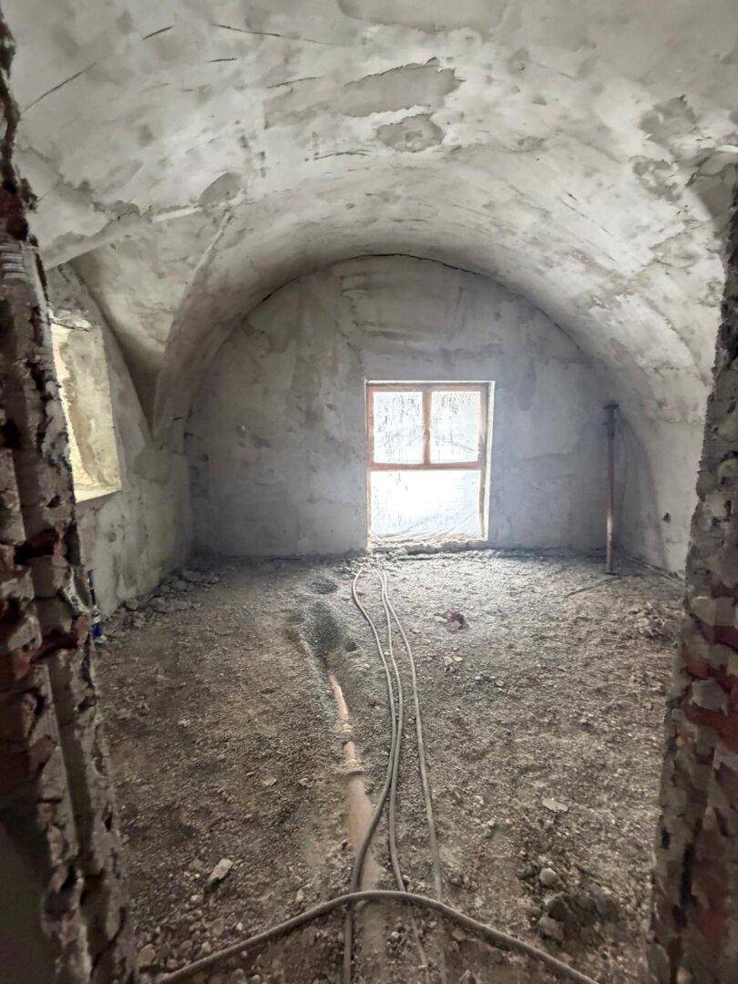 Raum im Rohbau mit gewölbter Decke, einem Fenster und vorbereitetem Boden für den Ausbau.