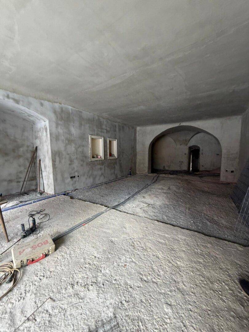 Großer, unfertiger Raum mit Betonboden, hohen Decken und gewölbten Durchgängen, bereit für den Ausbau.