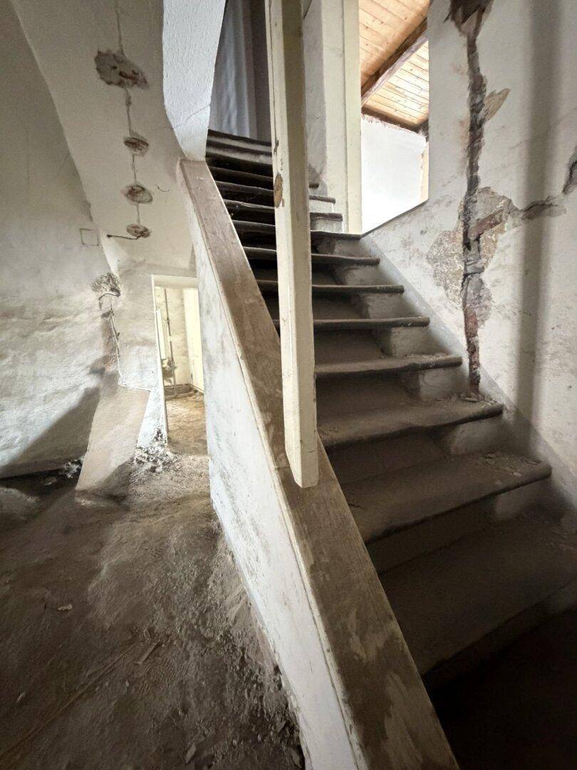 Alte Holztreppe in einem renovierungsbedürftigen Zustand, mit sichtbaren Schäden und freiliegenden Balken im Dachbereich.