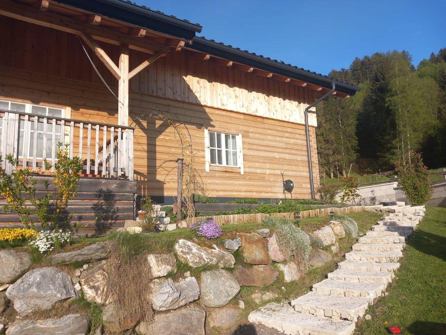 Gepflegter Gartenbereich mit Steintreppe, Felsen und blühenden Pflanzen neben dem Holzhaus.