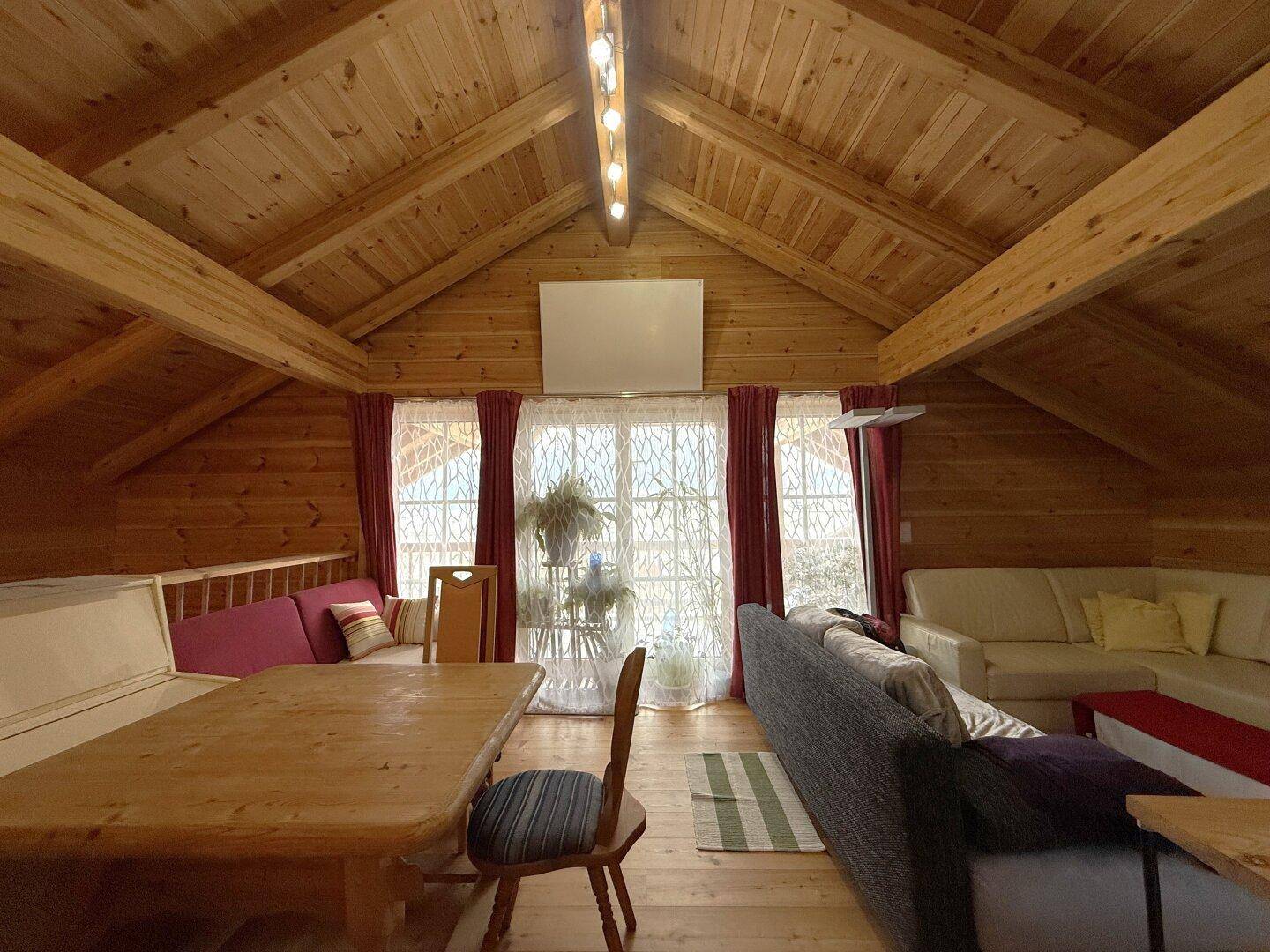 Geräumiges Wohnzimmer im Dachgeschoss mit Holzbalkendecke, großen Fenstern und Sitzbereichen.
