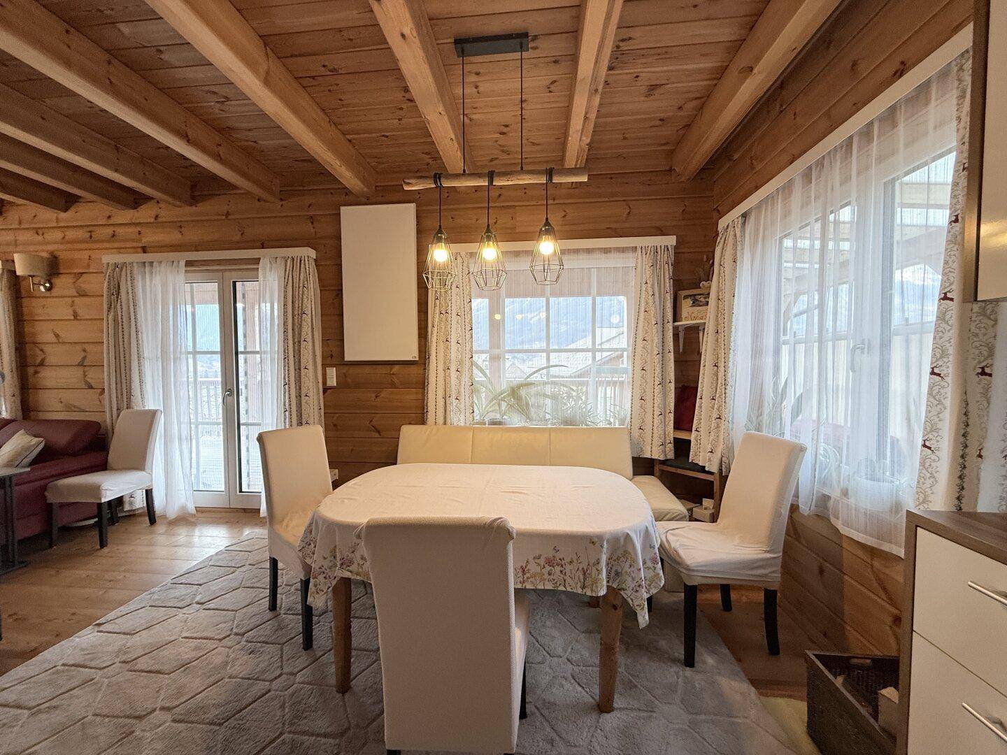 Gemütlicher Wohn-Essbereich mit Holzbalkendecke, Esstisch und großen Fenstern.