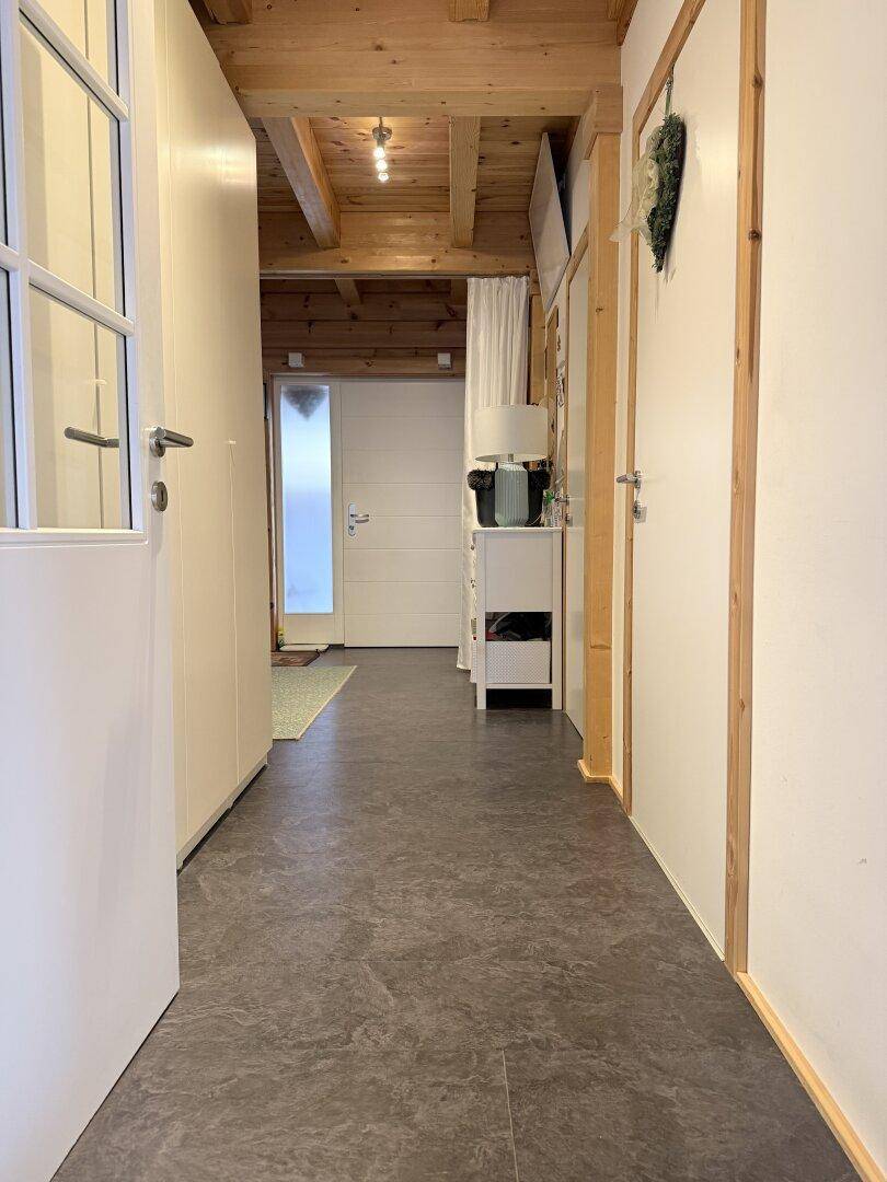 Heller Flur mit Holzbalkendecke und dunklem Boden, der zu weiteren Räumen führt.