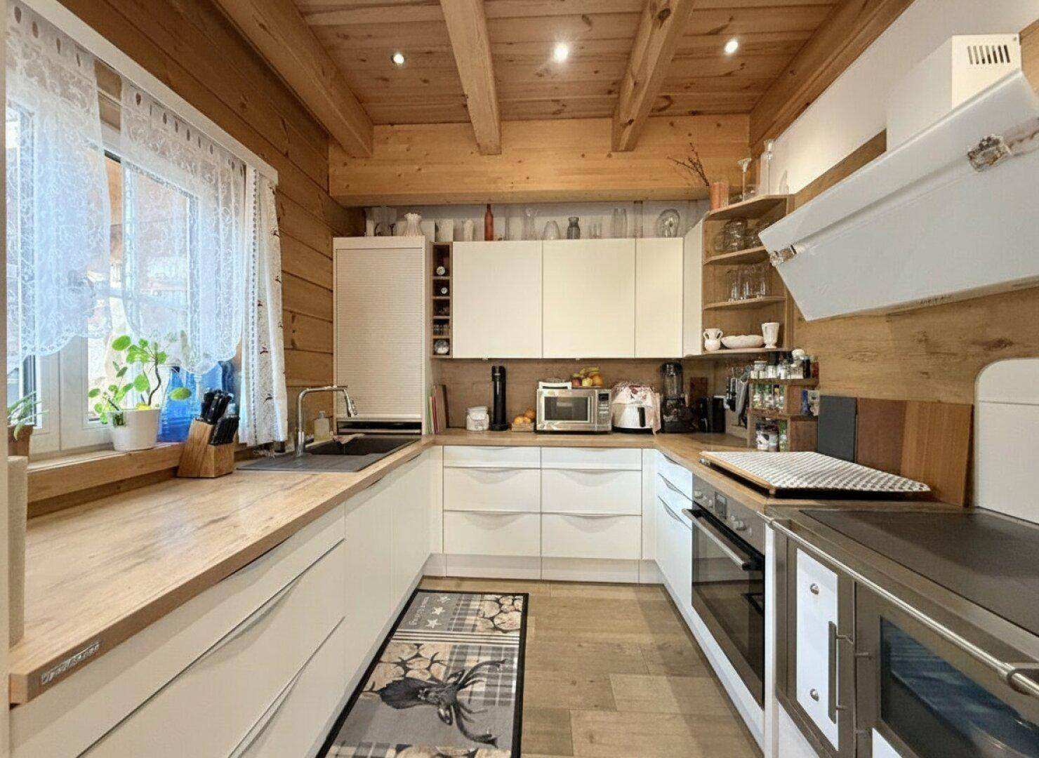 Moderne Holzküche mit weißen Schränken, Holzarbeitsplatten und sichtbaren Deckenbalken.