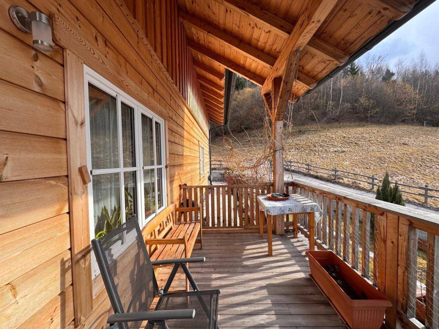 Gemütlicher Holzbalkon mit Sitzgelegenheiten und Blick auf die umliegende Landschaft und Hügel.