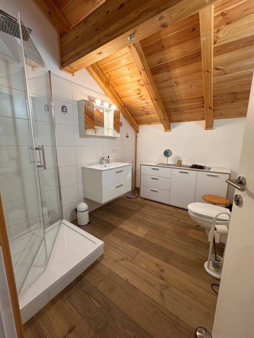 Helles Badezimmer im Dachgeschoss mit begehbarer Dusche, Waschtisch und Holzbalkendecke.