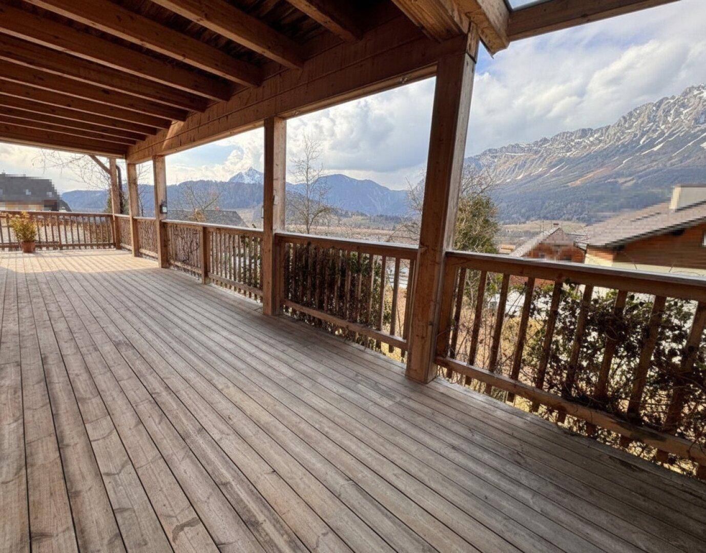 Geräumiger Holzbalkon mit weitem Blick auf die umliegende Berglandschaft und das Tal.