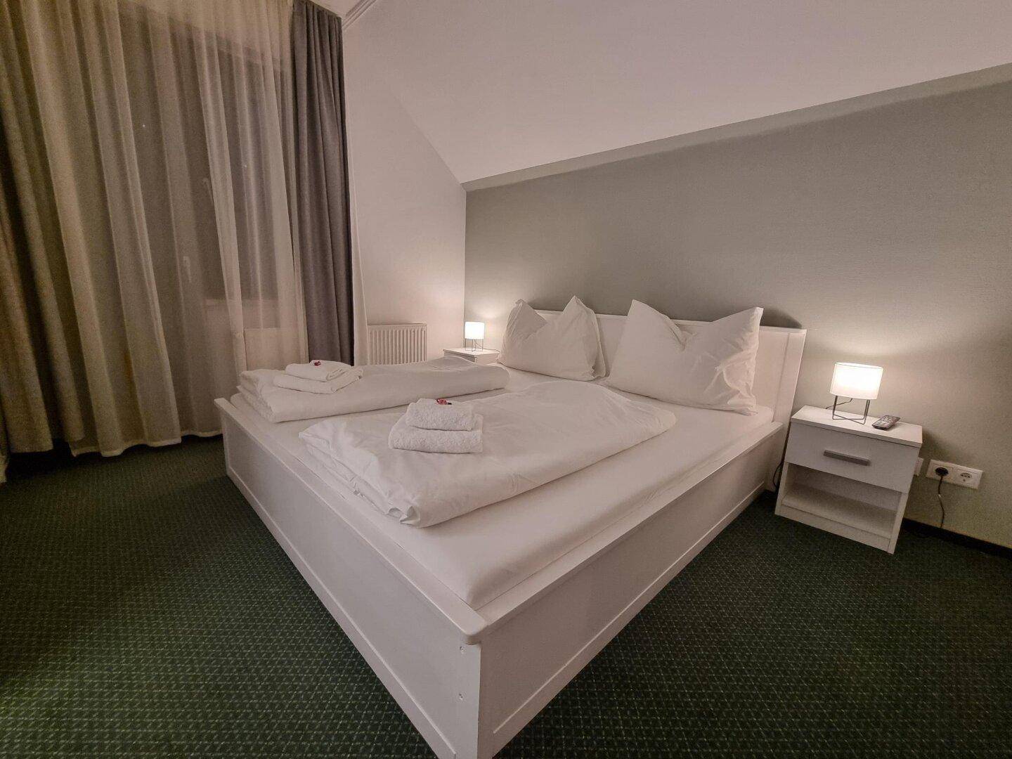 Helles Schlafzimmer mit einem großen weißen Doppelbett, Nachttischen und grüner Teppichboden.