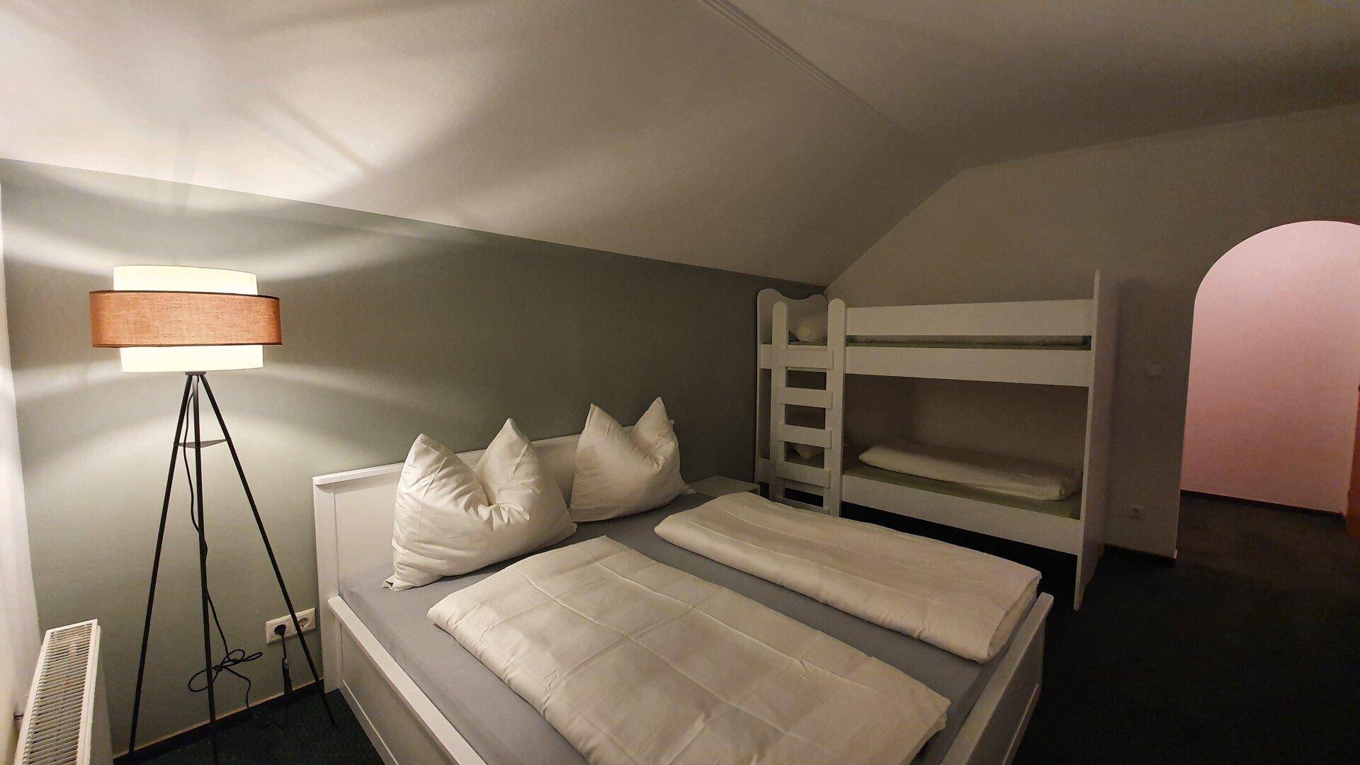 Schlafzimmer mit Doppelbett und Etagenbett, ideal für Familien, unter einer Dachschräge.