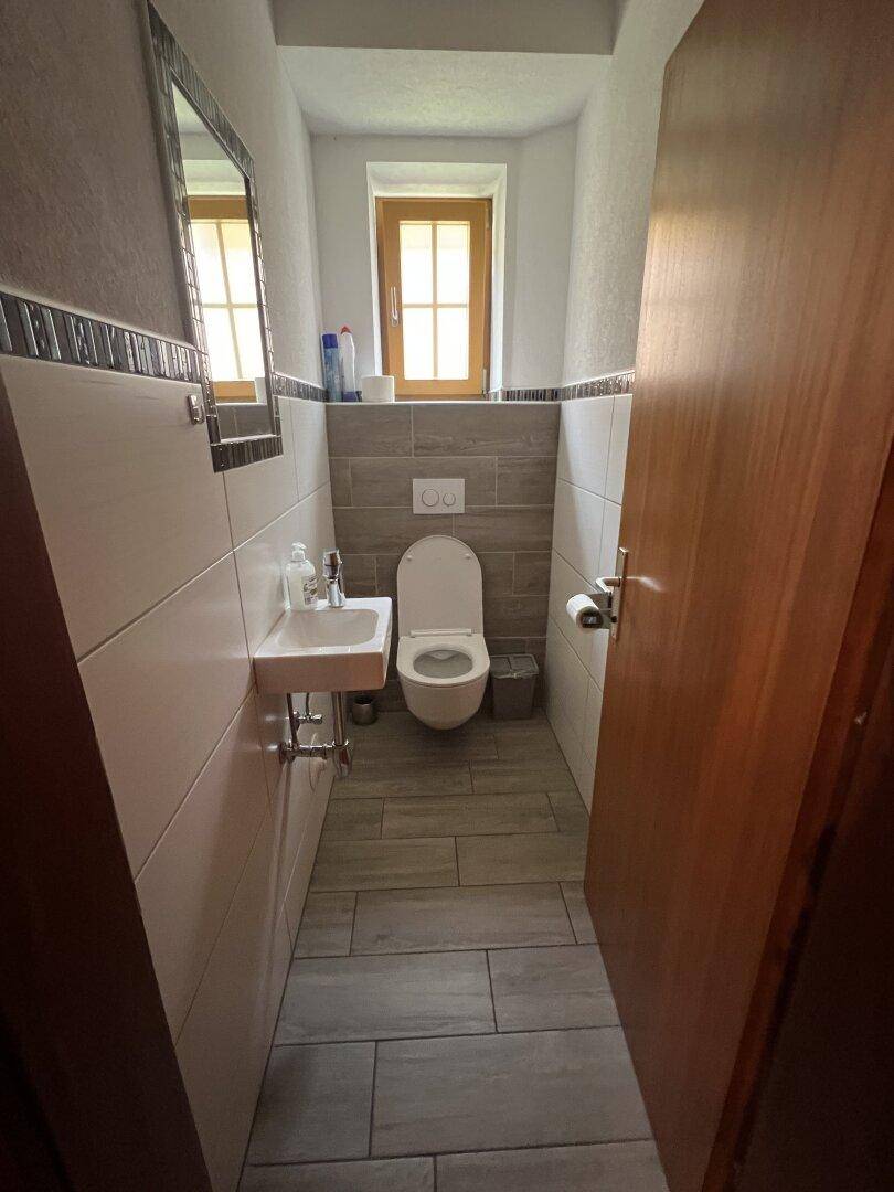 Kleines Gäste-WC mit wandhängendem WC, Einzelwaschbecken und einem Fenster für Tageslicht.