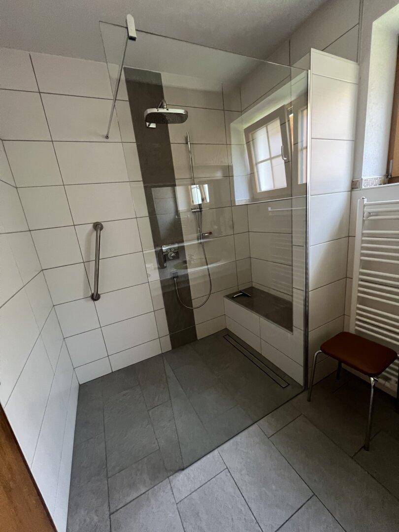 Modernes Badezimmer mit ebenerdiger Dusche, grauen und weißen Fliesen sowie einem Fenster.