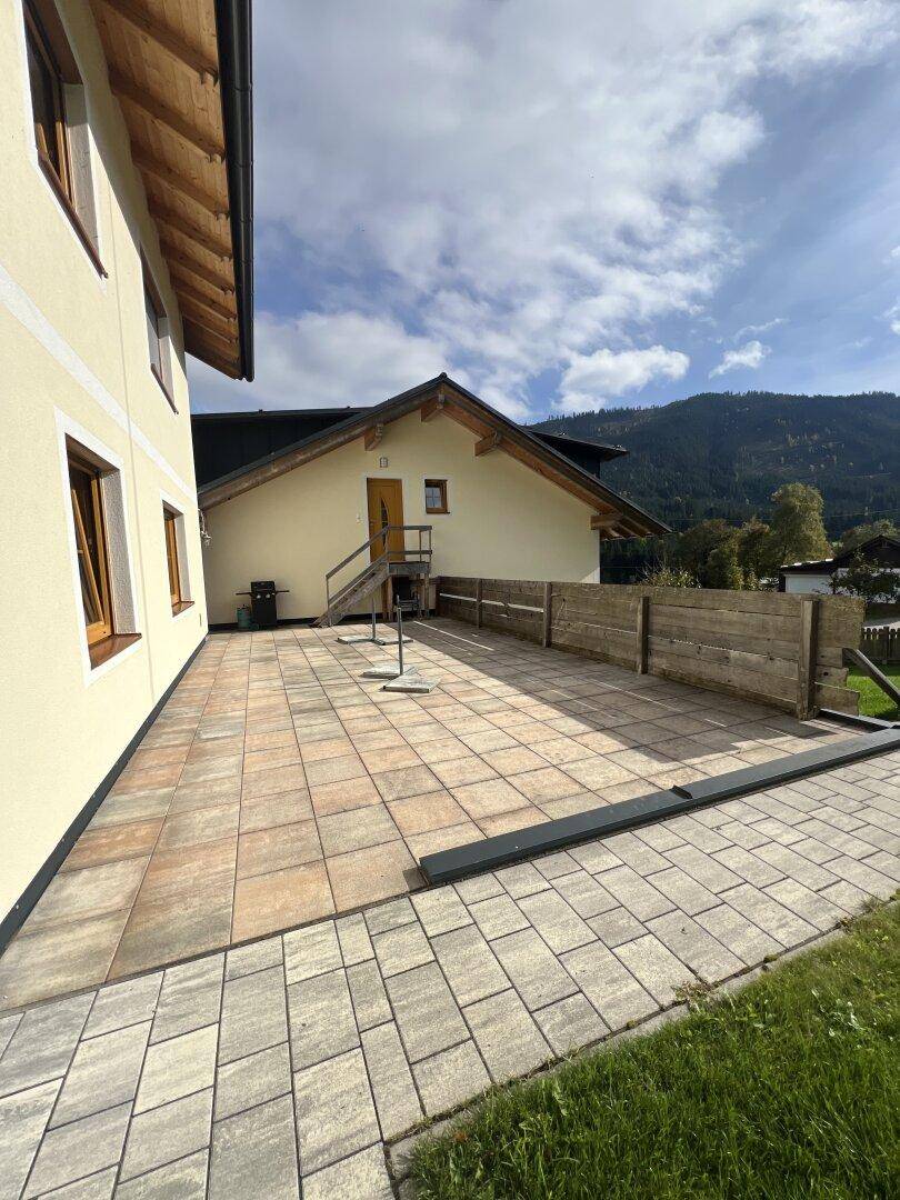 Große gepflasterte Terrasse am Haus mit Zugang über eine Holztreppe und Blick ins Grüne.